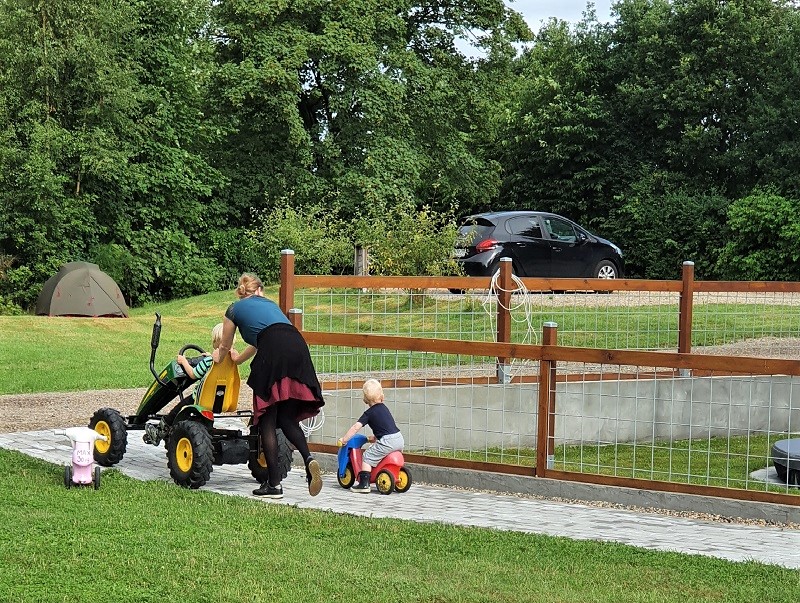 Mor skubber barn på pedelcart mens lillesøter kører på lille scooter 